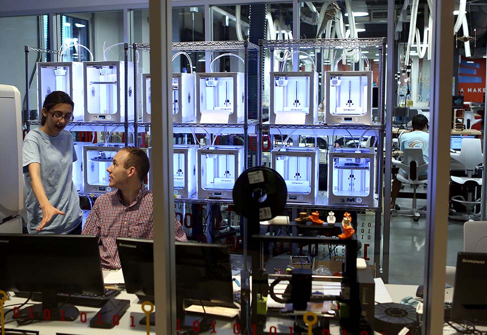 Image showing two students in the BeAM 3D printer room, discussing a project.